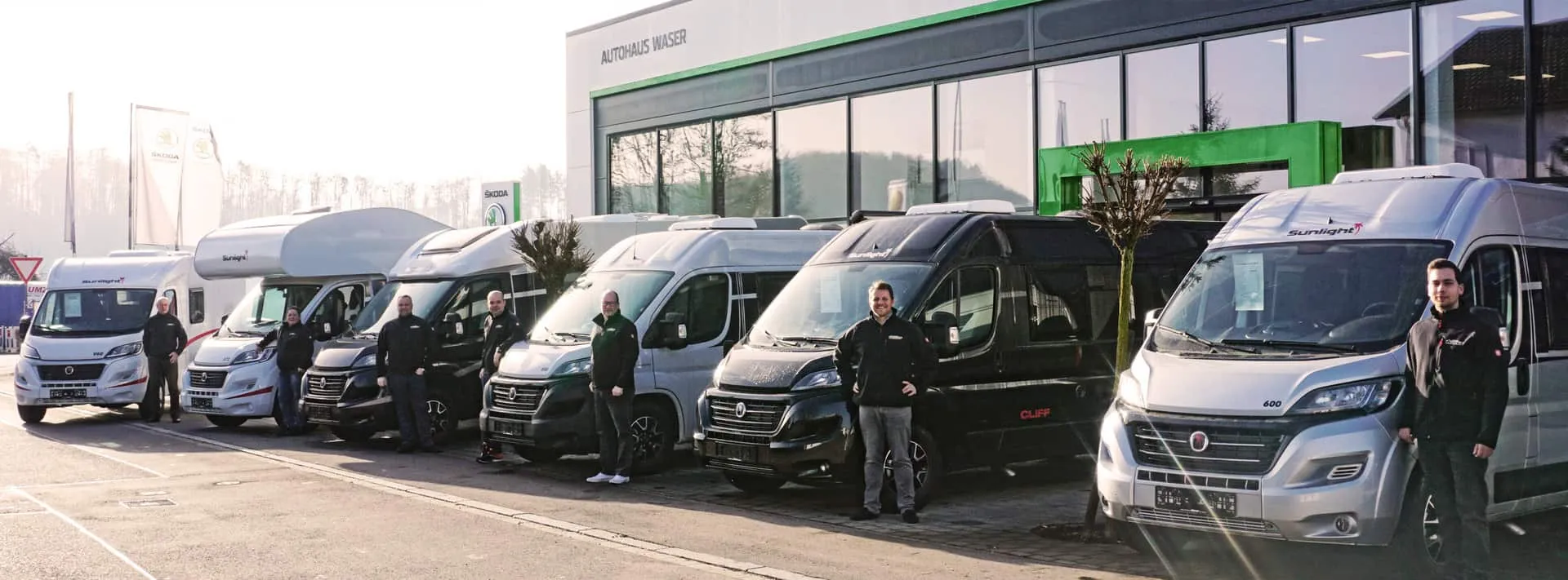 Eine Reihe von Sunlight Wohnmobilen mit Personen davor vor einem Autohaus.