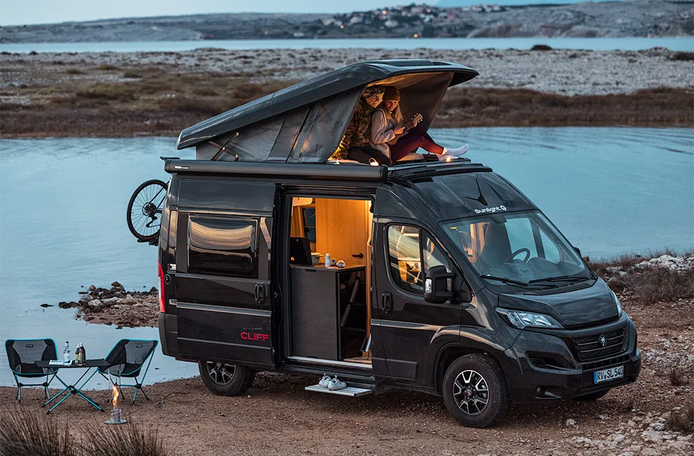 Campervan Sunlight Cliff am See mit Aufstelldach und Personen darin.