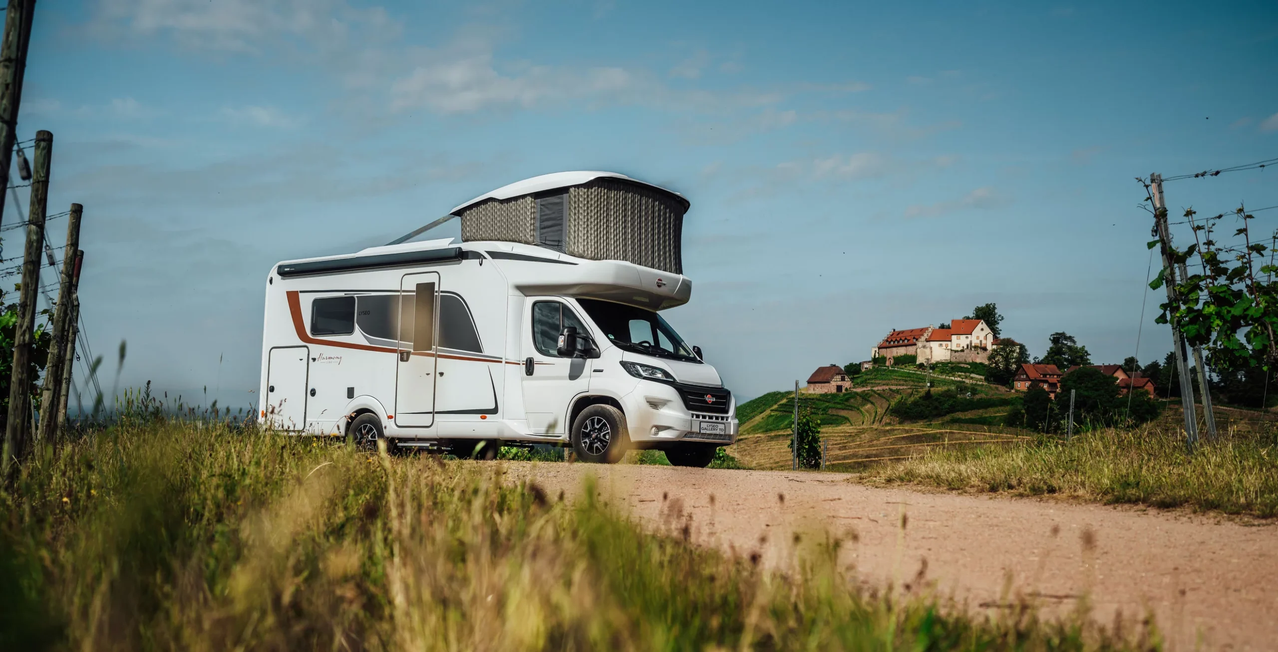 Wohnmobil der Marke Bürstner auf einem Feldweg vor einer ländlichen Kulisse.