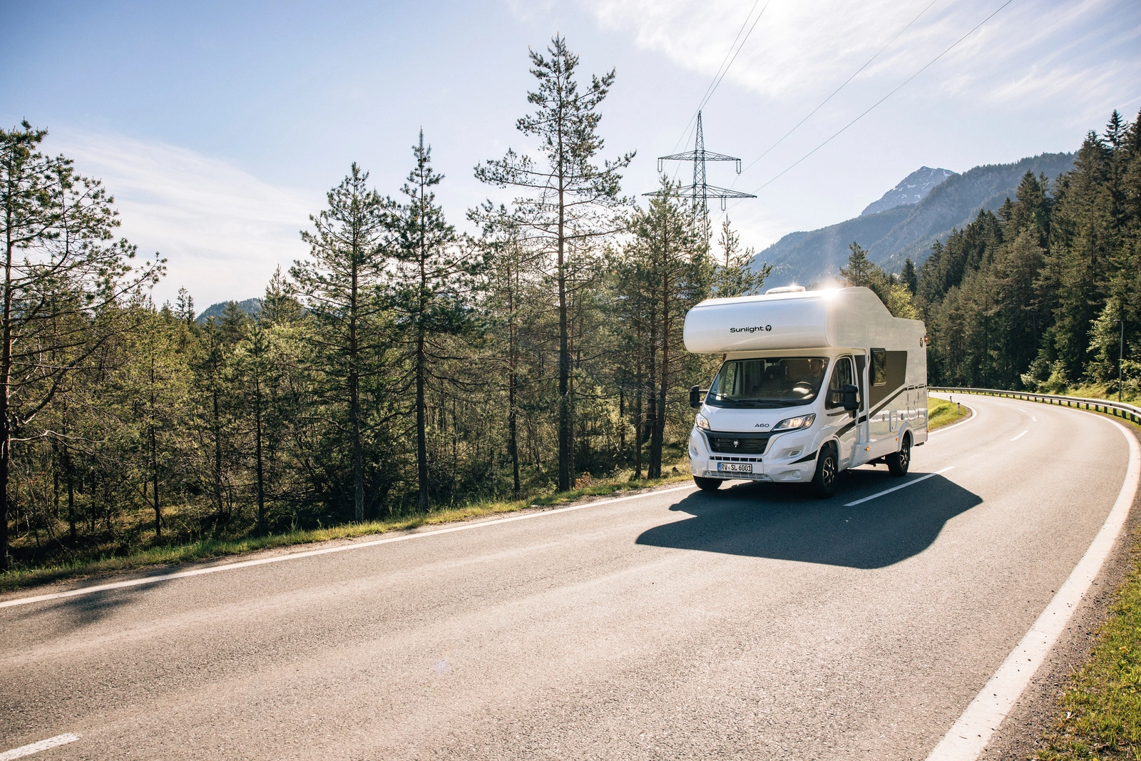 Ein Wohnmobil der Marke Sunlight fährt auf einer Landstraße durch eine bewaldete Berglandschaft.