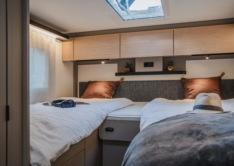 Innenansicht eines Camper-Schlafzimmers mit zwei Einzelbetten und Holzschränken.