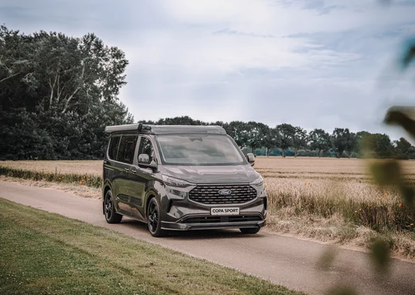 Ein Ford Copa Sport C500 Camper fährt auf einer Landstraße durch eine ländliche Umgebung.