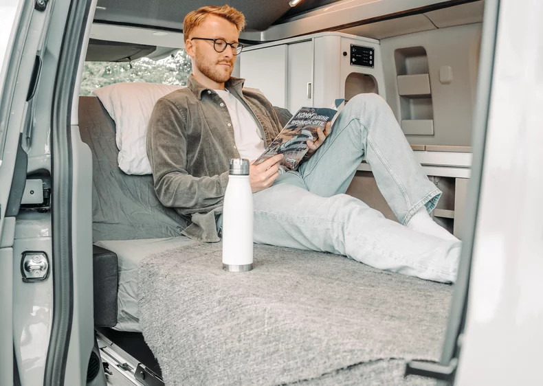 Ein Mann liest eine Zeitschrift auf einem Bett in einem Brüstner Copa Camper.