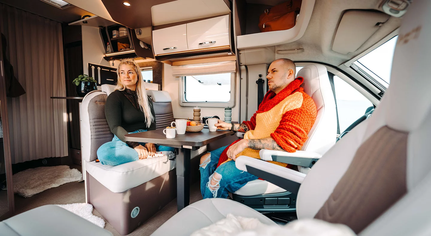 Zwei Personen sitzen in einem Wohnmobil an einem Tisch mit Getränken.