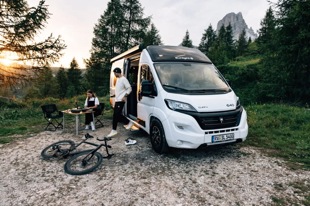 Zwei Personen campen neben einem Sunlight CLIFF X Wohnmobil in einer Waldlandschaft.