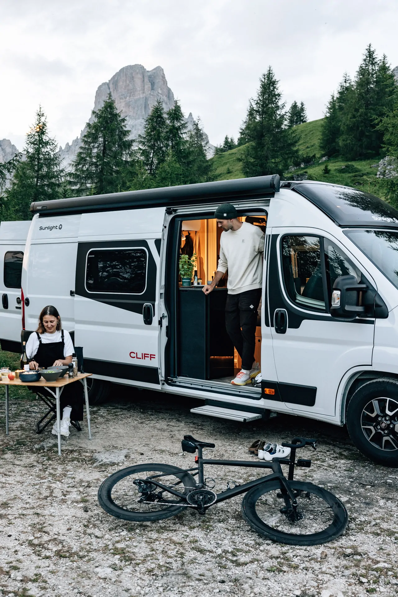 Ein Mann und eine Frau campen neben einem Sunlight CLIFF Wohnmobil in einer Berglandschaft.