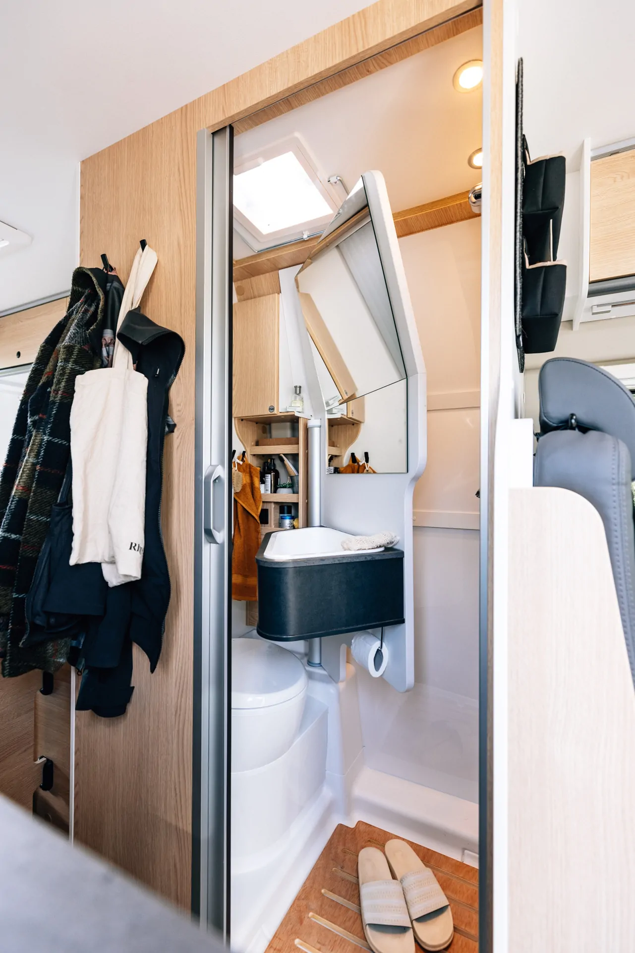 Innenansicht eines Cliff X Wohnmobils mit Bad, das eine Lamellentür, ein Waschbecken, eine Toilette und Regale zeigt.