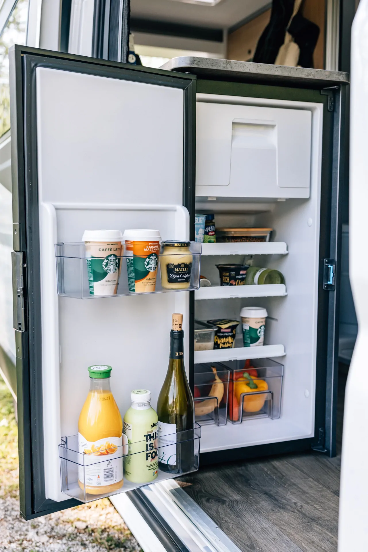Offener Kühlschrank in einem Camper mit Getränken und Lebensmitteln.