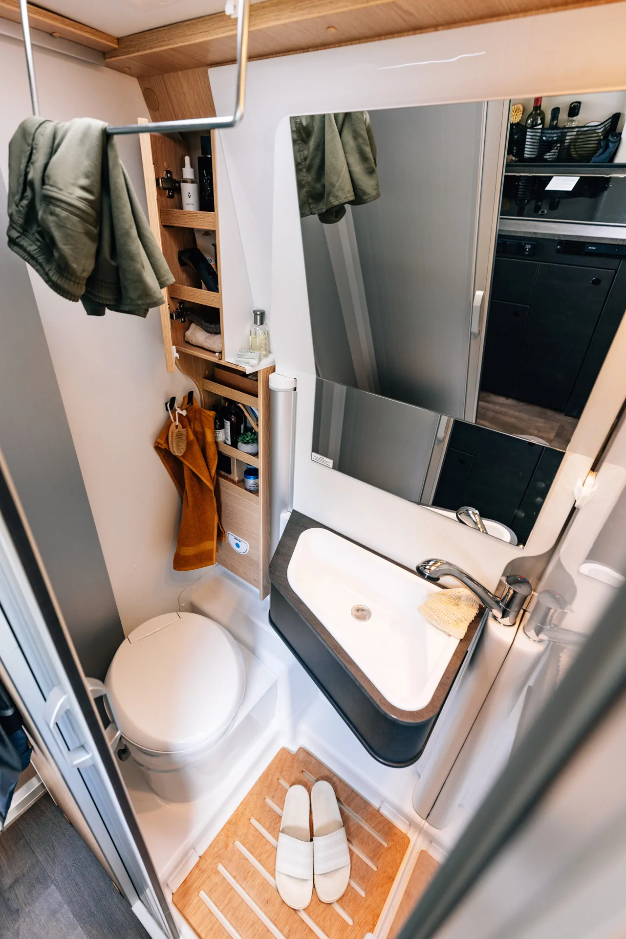 Kompaktes Badezimmer in einem Camper mit Toilette, Waschbecken und Regal.