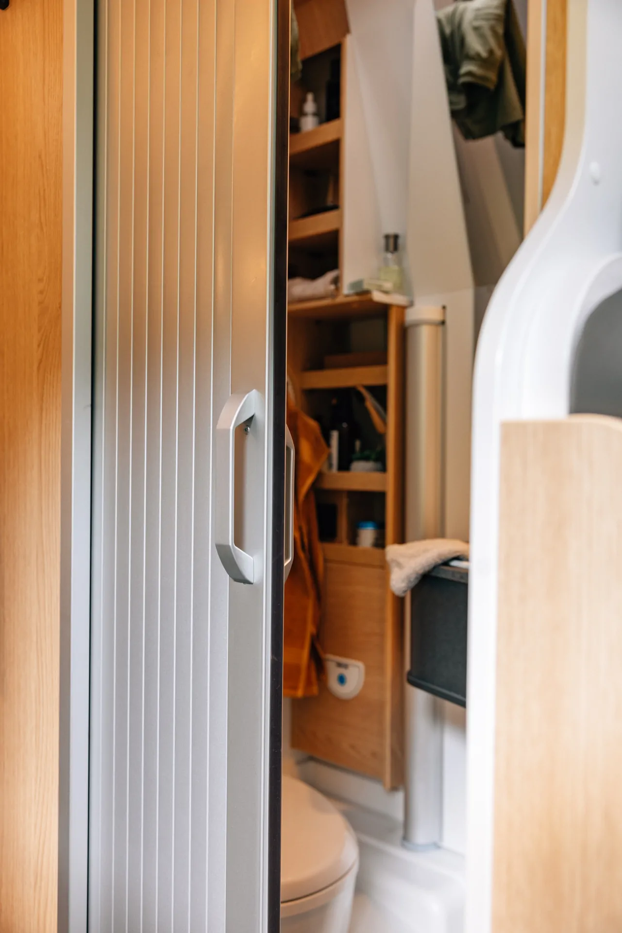 Innenansicht eines Camperbads mit geöffneter Schiebetür und sichtbarer Toilette.