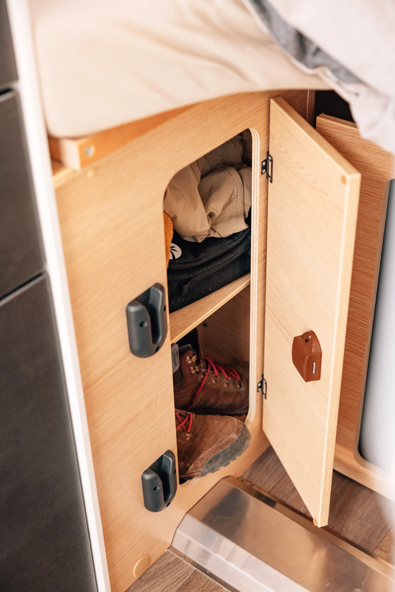 Offenes Holzfach in einem Camper mit Kleidung und Wanderschuhen.