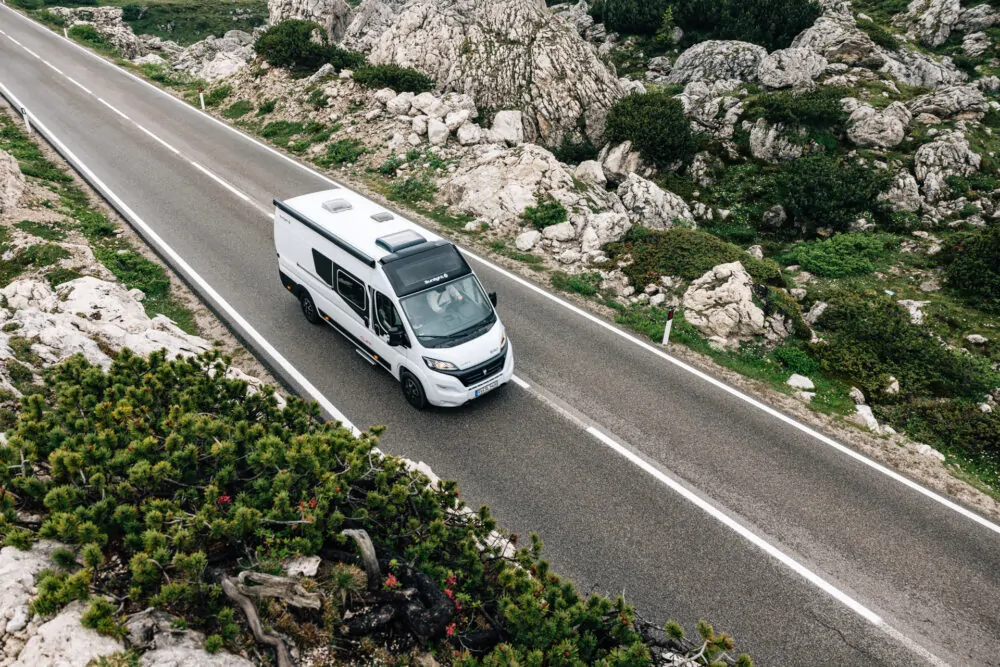 Ein Campervan fährt auf einer kurvenreichen Straße durch eine felsige Landschaft.