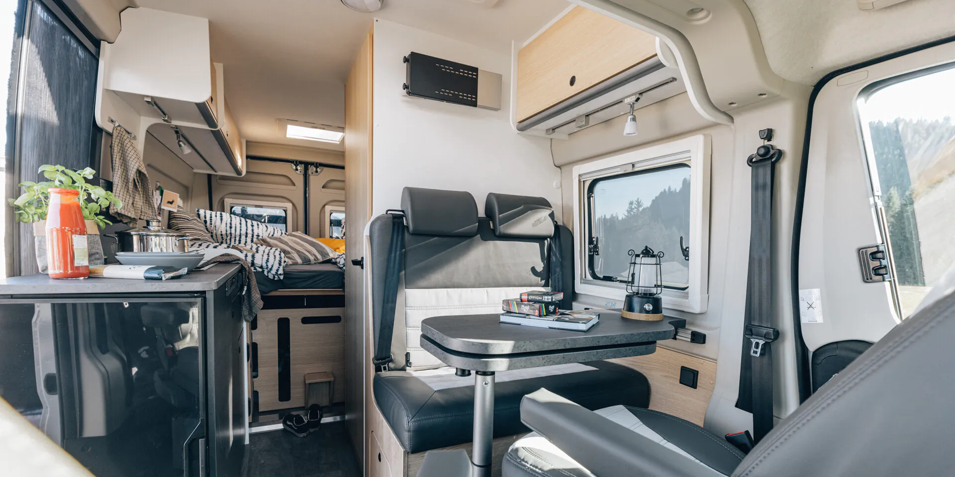 Innenansicht eines Cliff 602 Adventure Wohnmobils mit Tisch, Sitzbank, Küche und Schlafbereich.