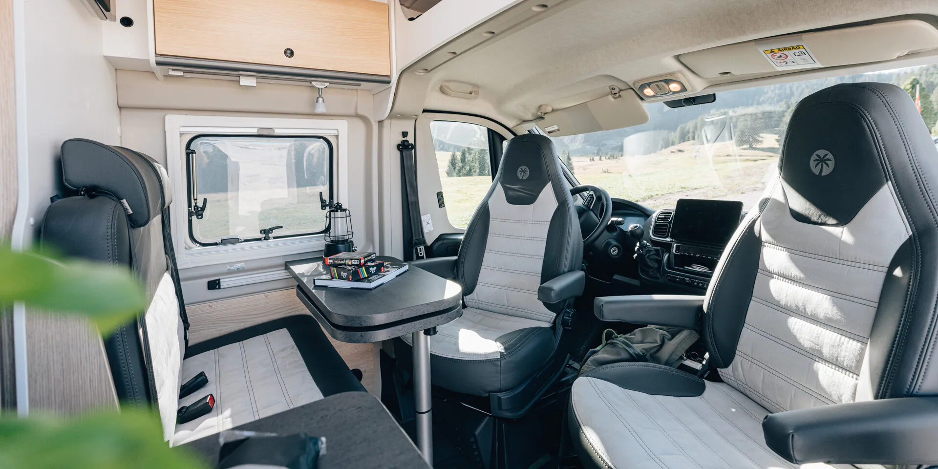 Innenraum eines Campervans mit Tisch, zwei drehbaren Sitzen und einem Fenster.