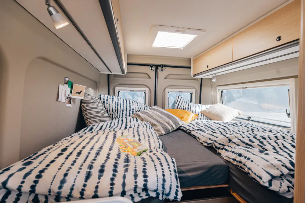 Innenraum eines Wohnmobils mit gemütlichem Bett und dekorativen Kissen.