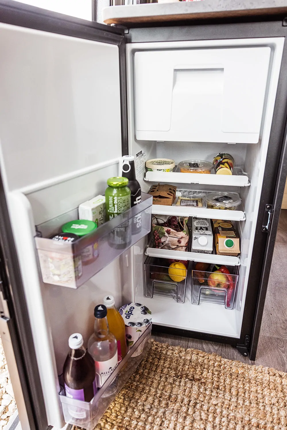 Offener Kühlschrank mit verschiedenen Lebensmitteln und Getränken gefüllt.