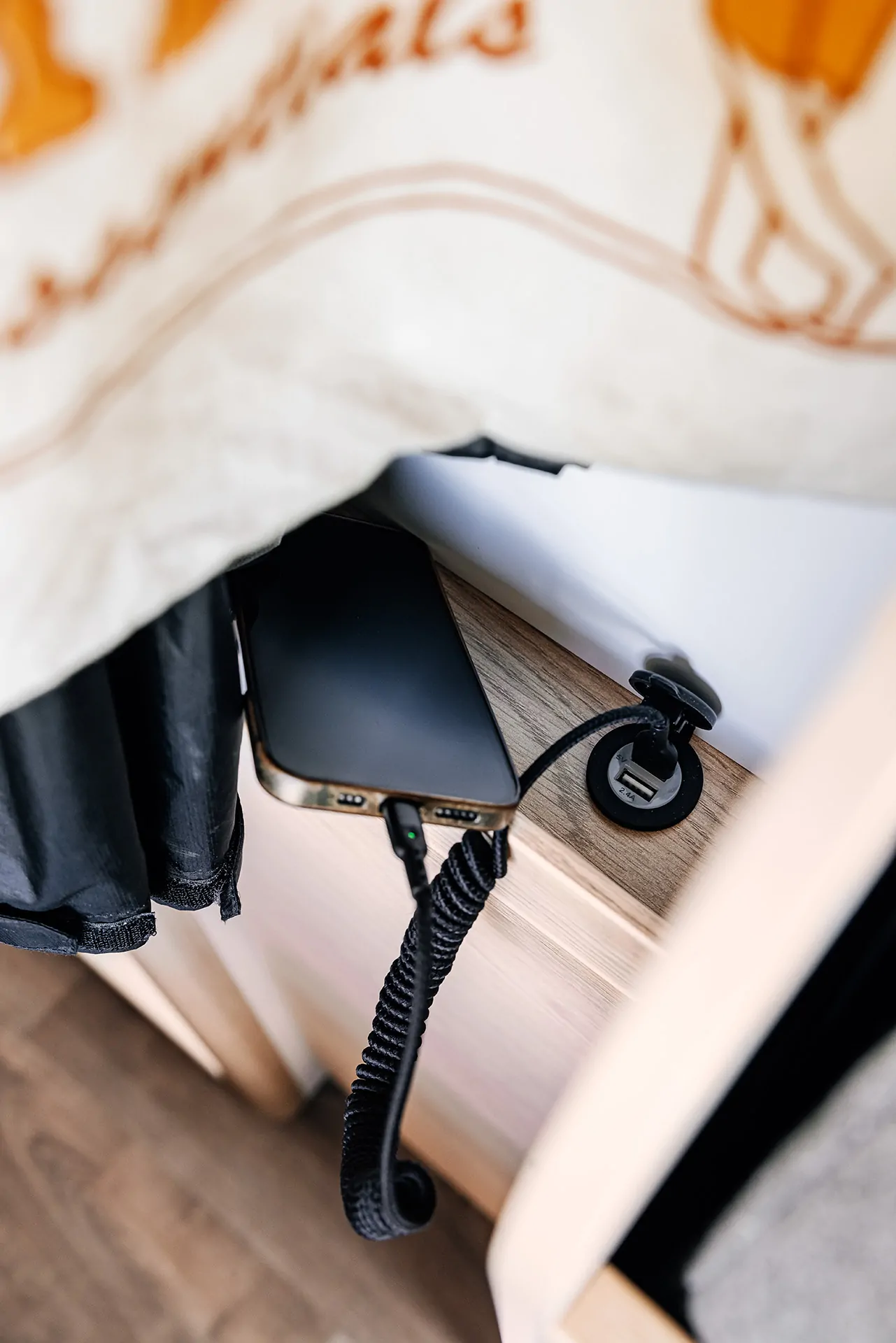 Ein Smartphone wird über ein USB-Kabel auf einem Holztisch aufgeladen.