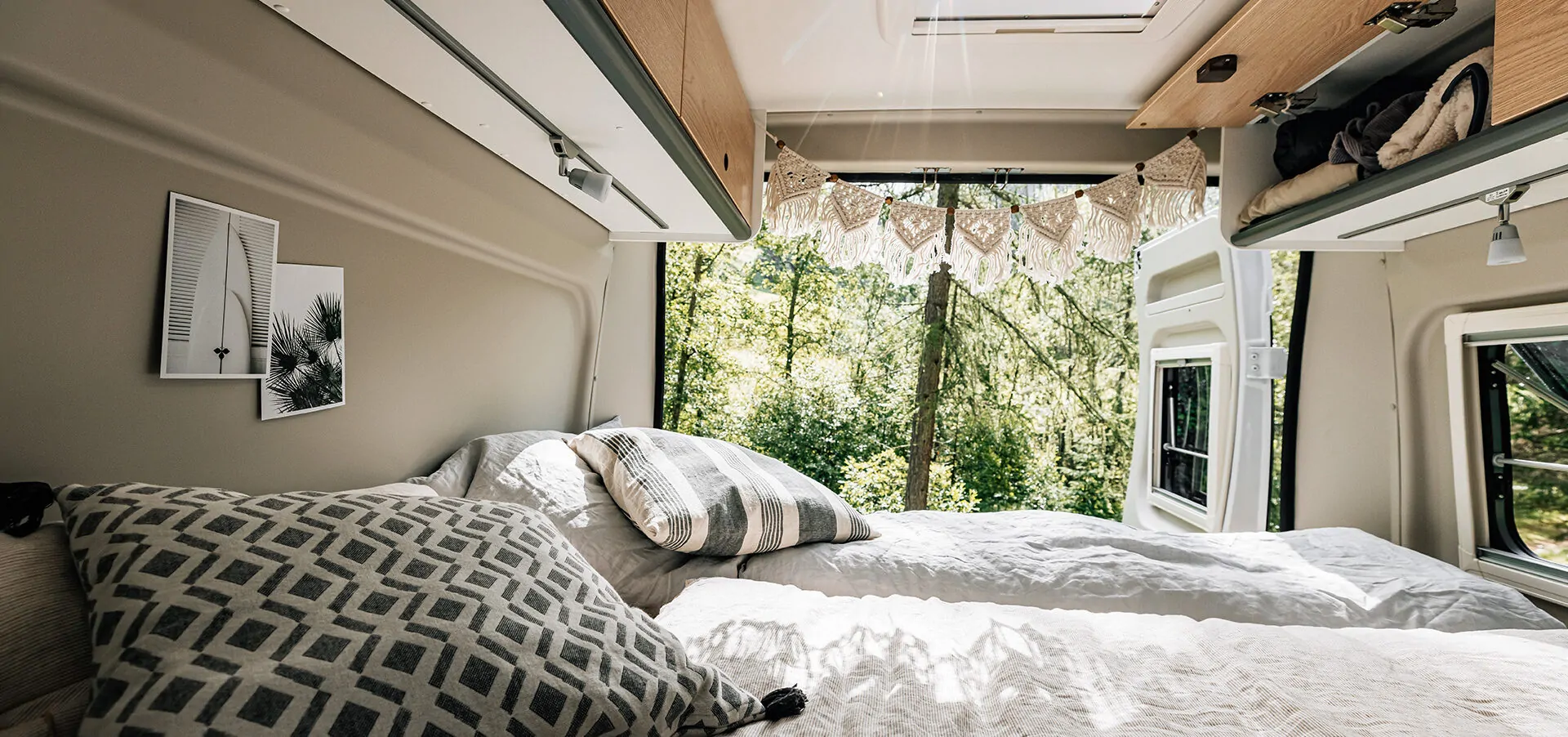 Interieur eines Campers mit gemütlichem Bett und Blick nach draußen in die Natur.