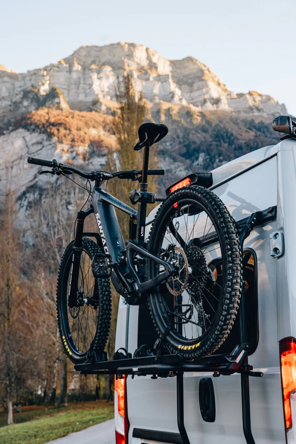 Ein Mountainbike ist auf einem Fahrradträger am Heck eines Campers vor einer Bergkulisse befestigt.