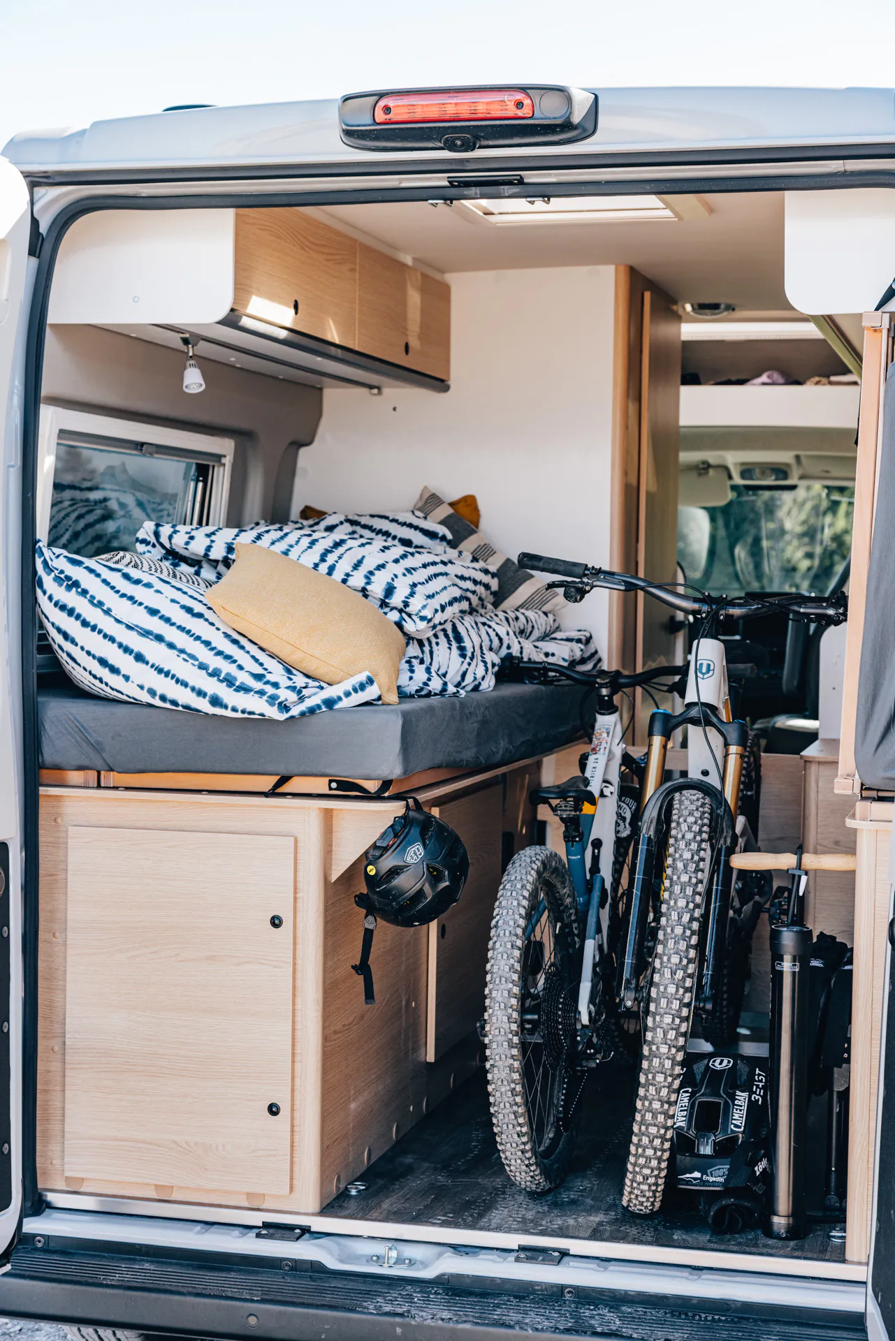 Der geöffnete Kofferraum eines Campers zeigt ein Bett mit Kissen und zwei Fahrräder.