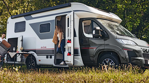 Ein Bürstner Lyseo Time T 726 Wohnmobil steht auf einer Wiese, während eine Frau einsteigt.