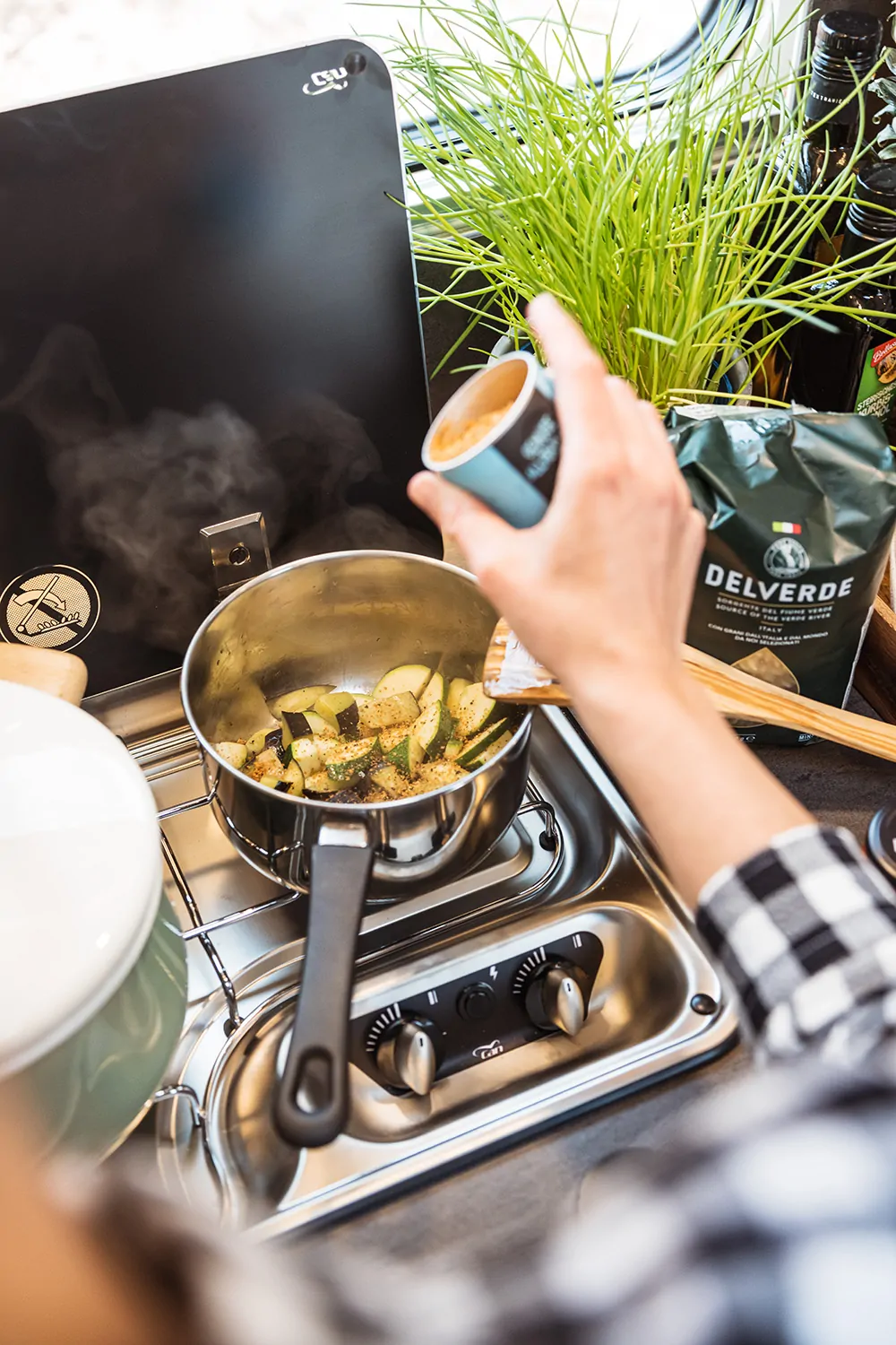 Eine Person würzt in einer Camperküche Gemüse in einem Topf.