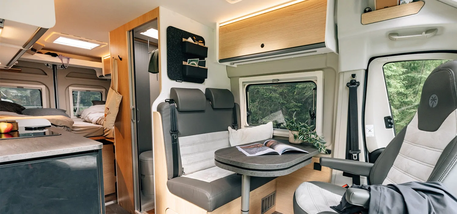 Innenansicht eines Sunlight Cliff X Wohnmobils mit Sitzbereich, Tisch und Bett im Hintergrund.