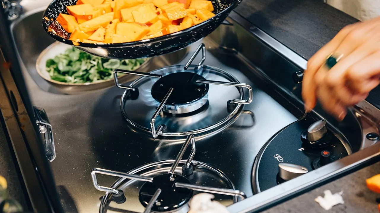 Gasherd in einer Camperküche mit Pfanne voller Kürbisstücke.