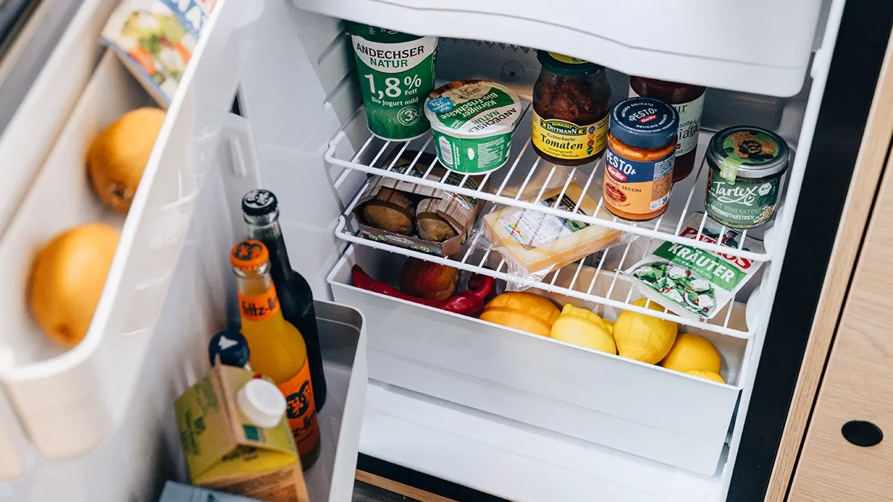 Offener Kühlschrank mit verschiedenen Lebensmitteln, darunter Joghurt, Käse und Getränke.