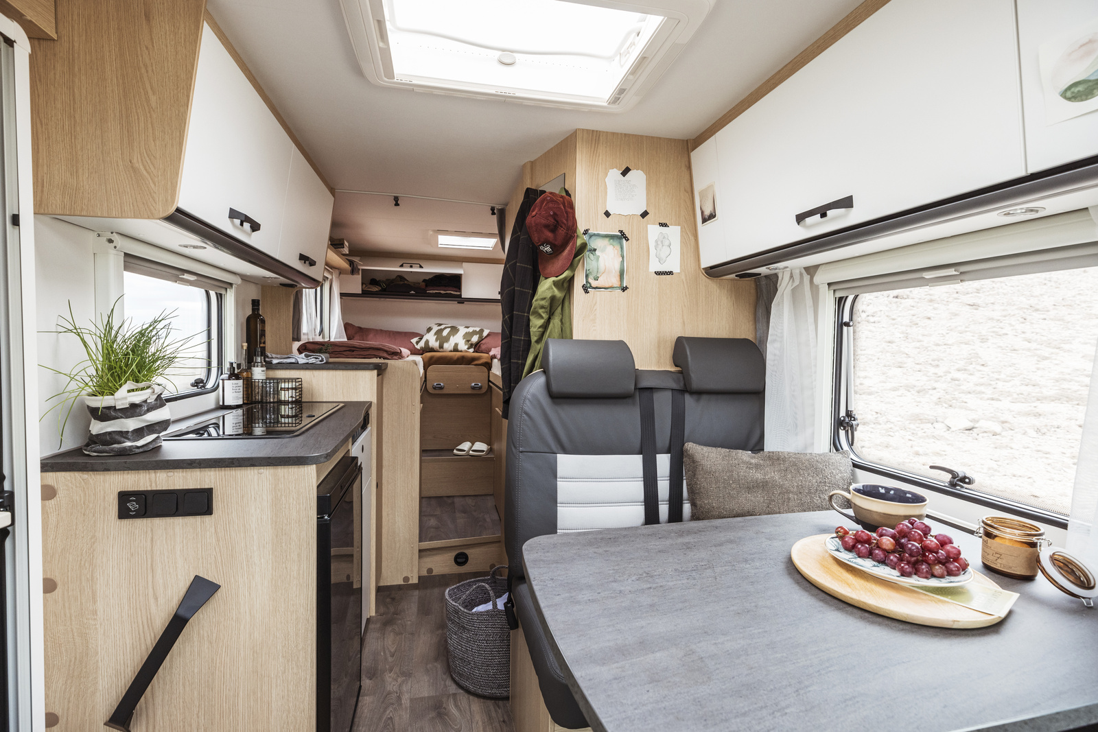 Innenansicht eines modernen Wohnmobils mit Küche, Esstisch und Schlafbereich.