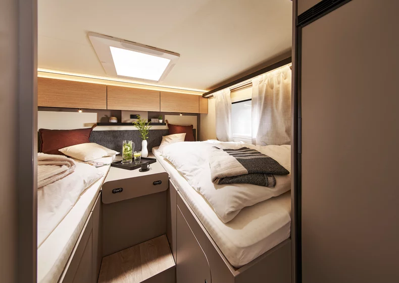 Innenansicht eines Bürstner Campeo Wohnmobilschlafzimmers mit zwei Einzelbetten und einem Dachfenster.