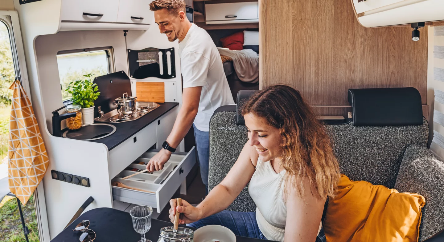 Eine Frau und ein Mann bereiten gemeinsam Frühstück in einem Bürstner Lyseo Time Skyline Wohnmobil zu.