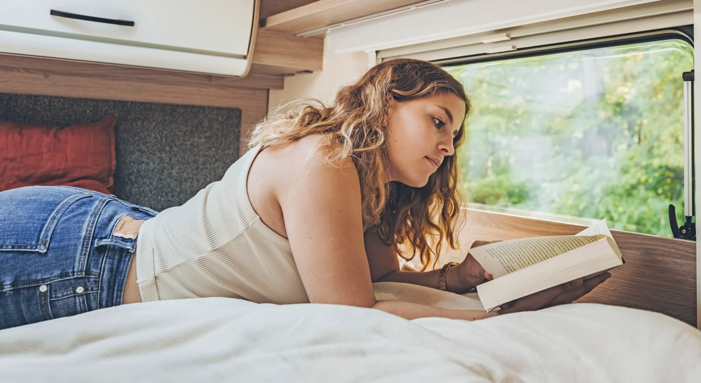 Eine Frau liest ein Buch im Bett eines Bürstner Lyseo Time Wohnmobils.