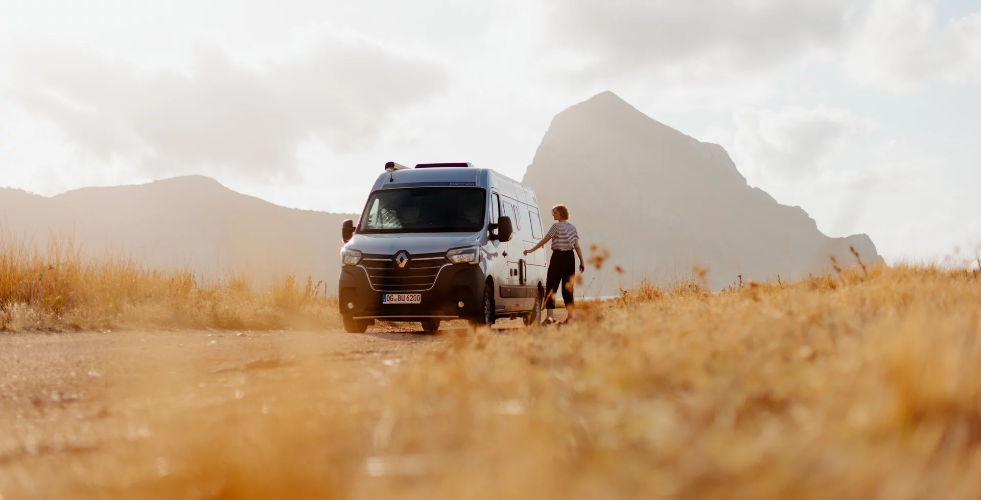 Frau neben einem Bürstner Delfin Camper in einer Landschaft mit Bergen.