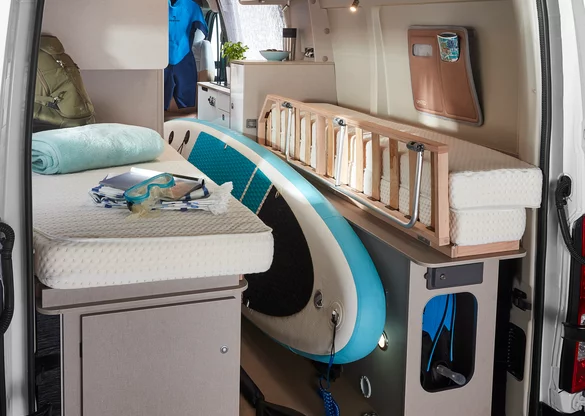 Innenansicht eines Bürstner Delfin C 621 Wohnmobils mit Bett, Surfbrett und Tauchzubehör.