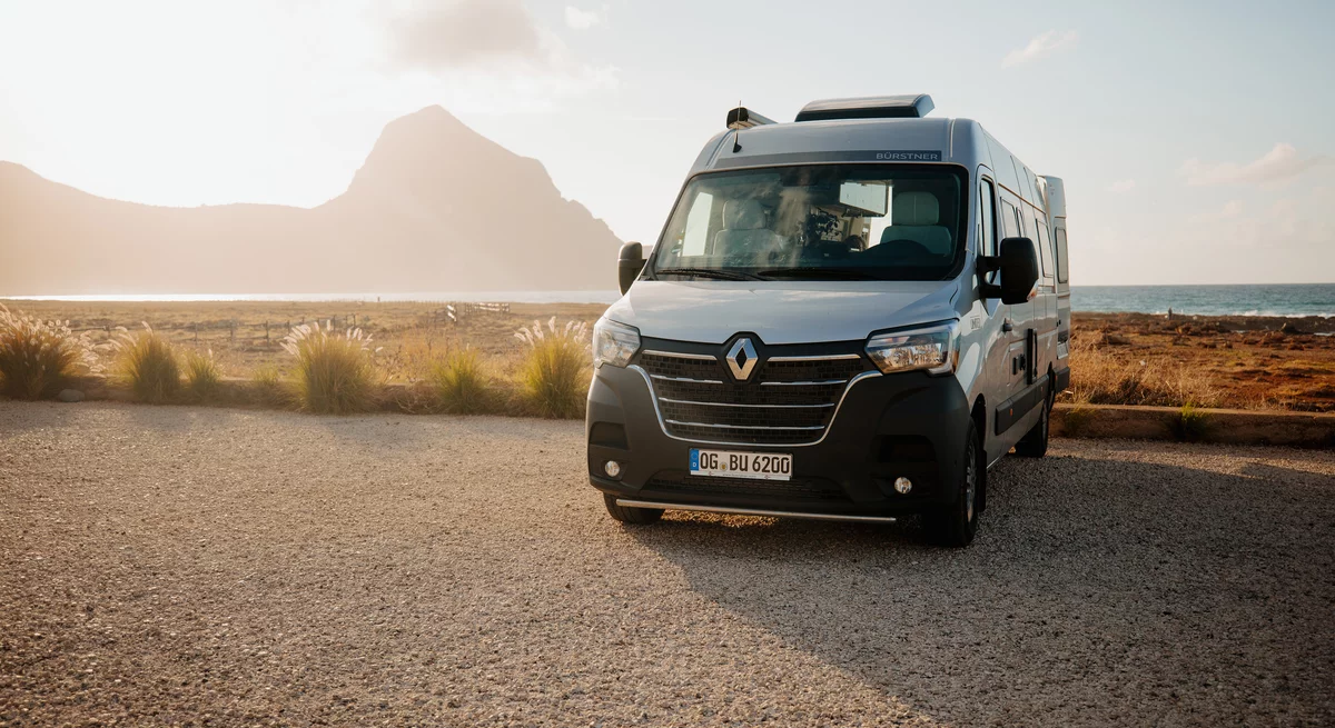 Ein Bürstner Wohnmobil steht auf einem Parkplatz mit Blick auf eine Küstenlandschaft bei Sonnenuntergang.