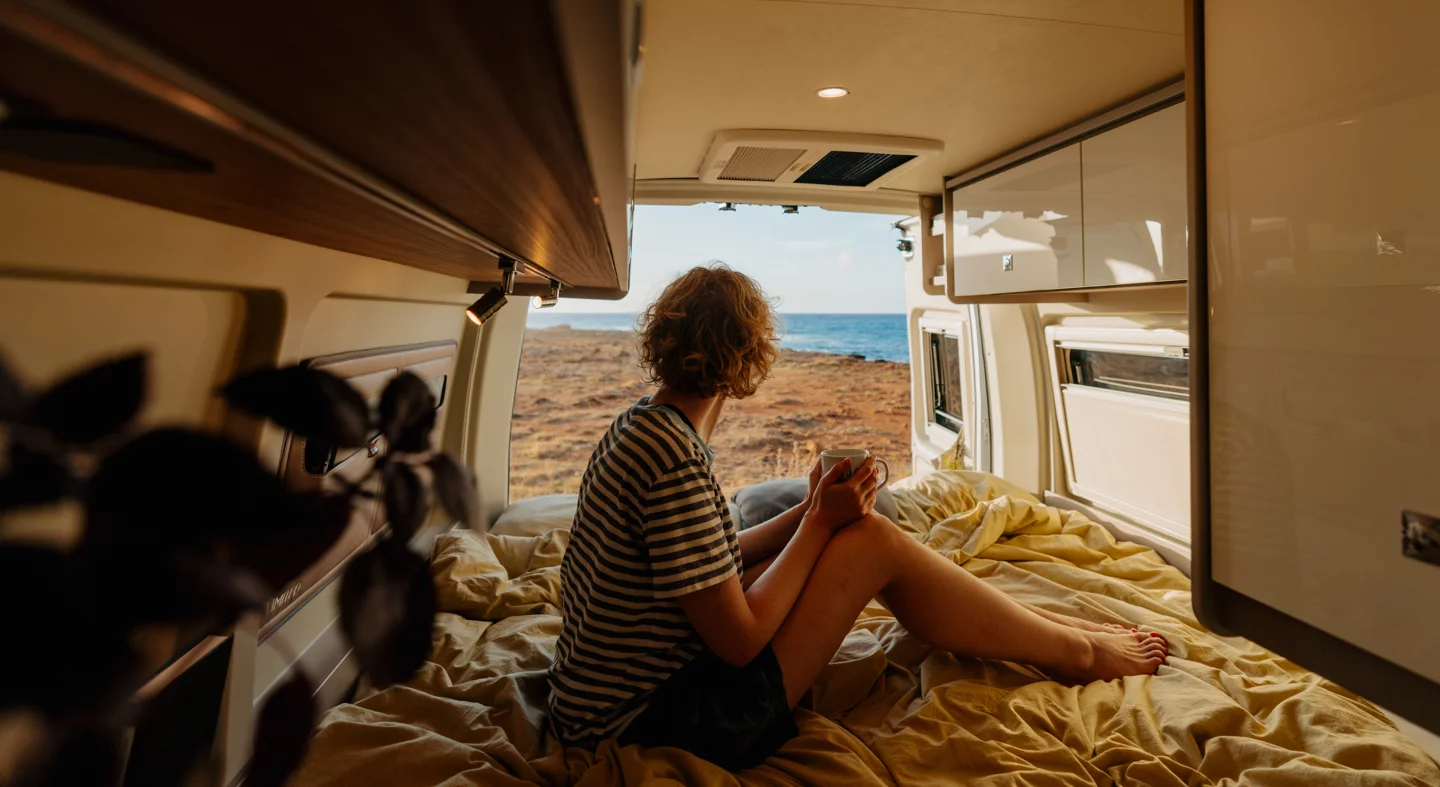 Eine Person sitzt im Inneren eines Wohnmobils und blickt auf das Meer.