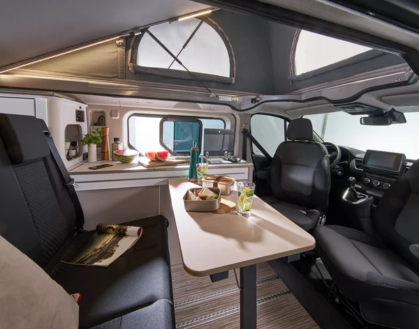 Innenansicht eines Bürstner Playa C500 Wohnmobils mit Tisch, Sitzbereich und Küchenzeile.