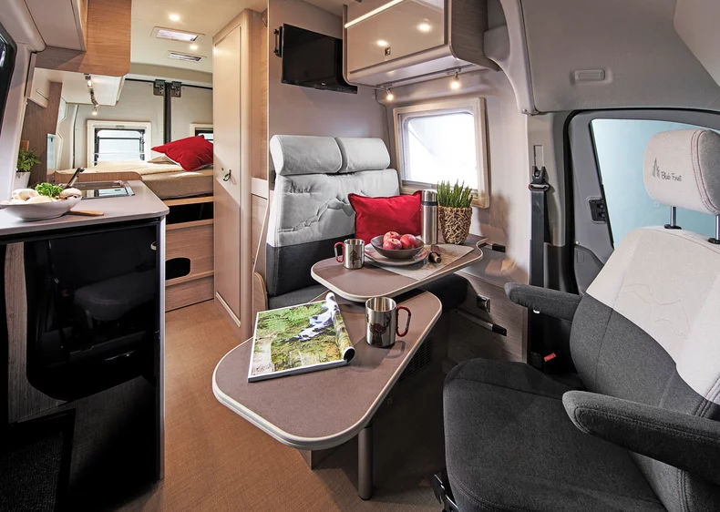 Innenraum eines Bürstner Lineo 4x4 C590 Campers mit Sitzbereich, Tisch und Küche.