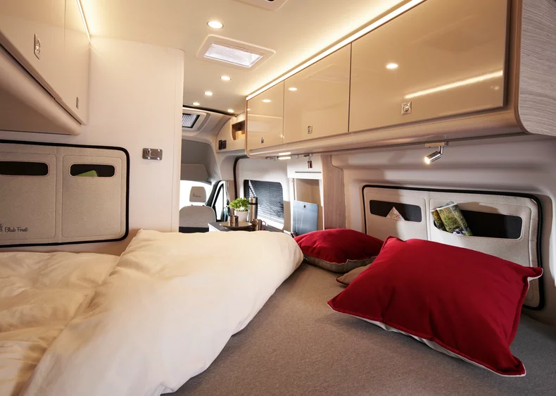 Innenansicht eines Bürstner Lineo 4x4 C590 Campers mit Bett, roten Kissen und Schränken.