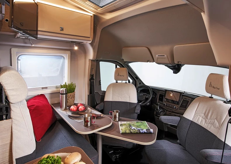 Innenraum eines Bürstner Lineo C 590 Wohnmobils mit Tisch, zwei Sitzen und dekorativen Elementen.