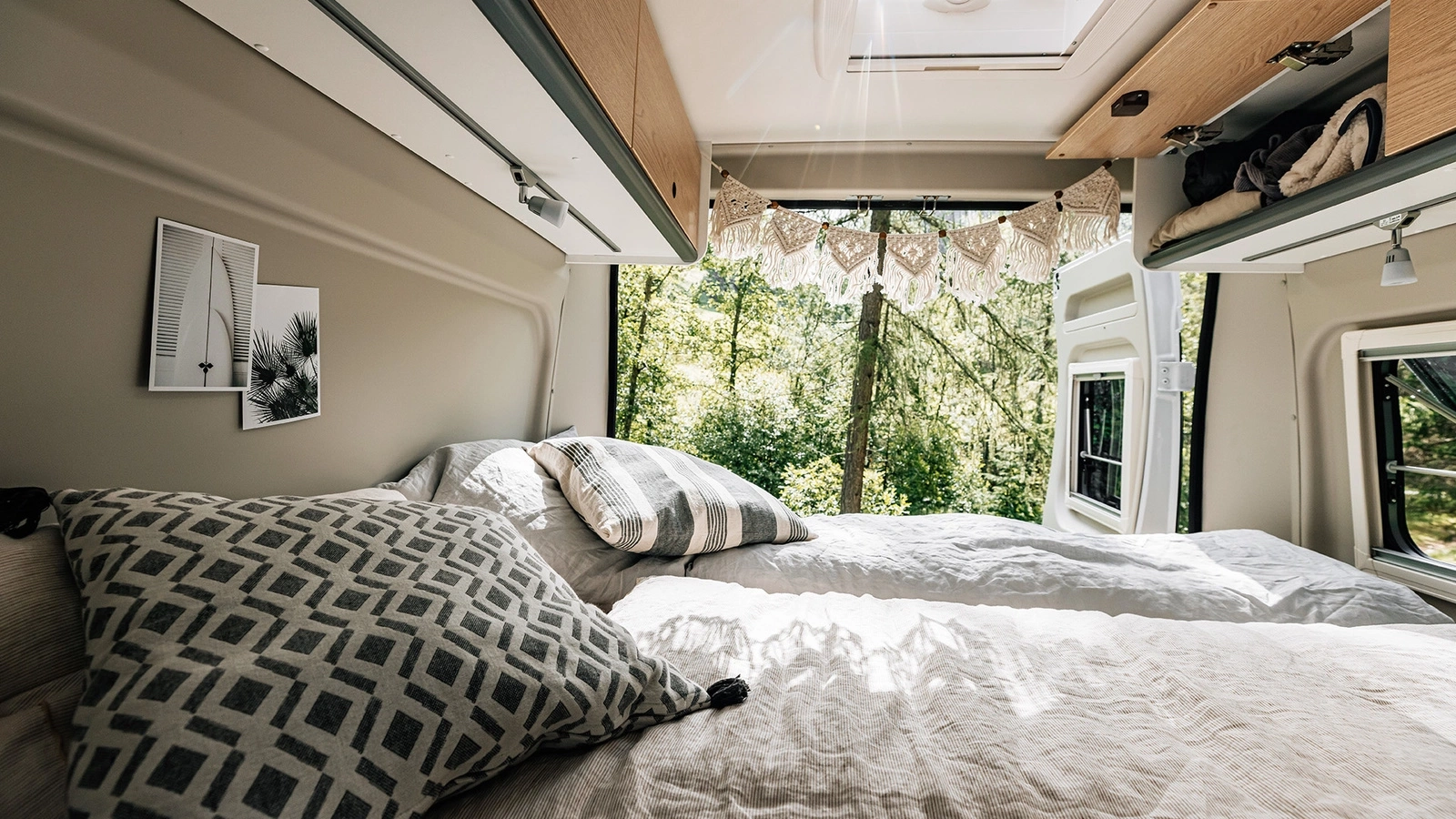 Innenansicht eines Peugeot Campervans mit gemütlichem Bett, dekorativen Kissen und Blick ins Grüne.