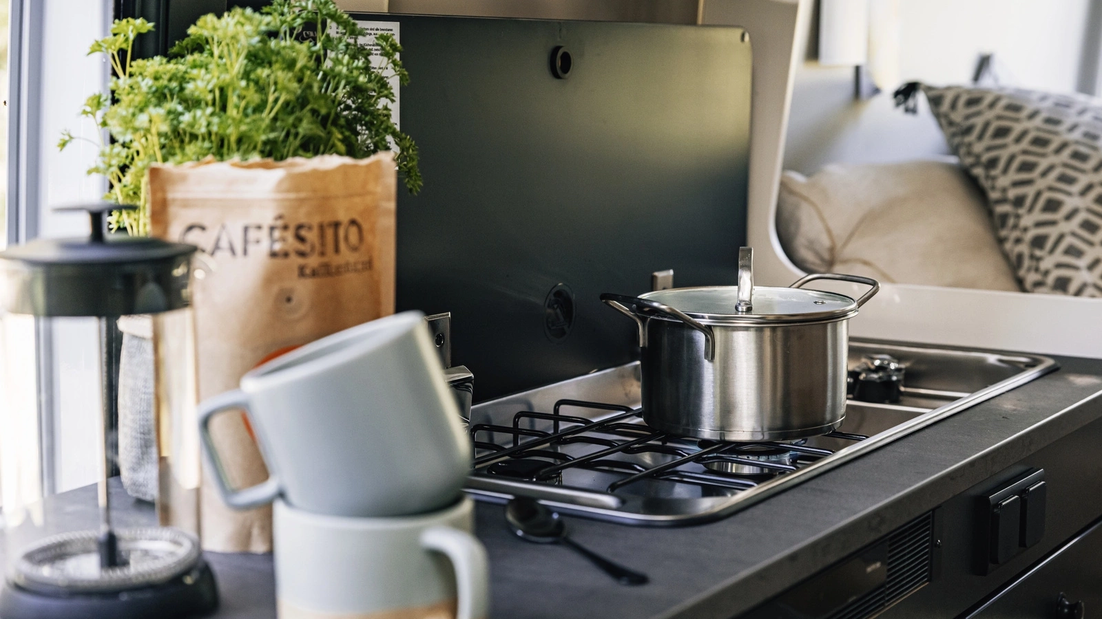 Küchenzeile in einem Peugeot Camper mit Kochtopf, Tassen und Kräutern.