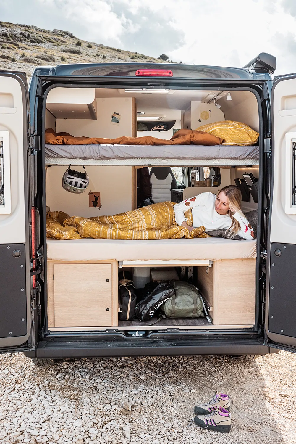 Eine Frau liegt in einem geöffneten Camper, vermutlich ein Cliff 601, auf einem Bett.
