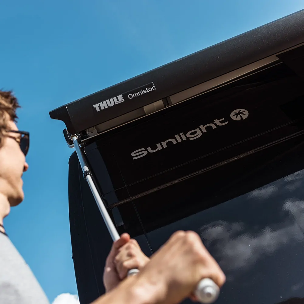 Eine Person kurbelt eine Thule Omnistor Markise an einem Sunlight-Fahrzeug aus.