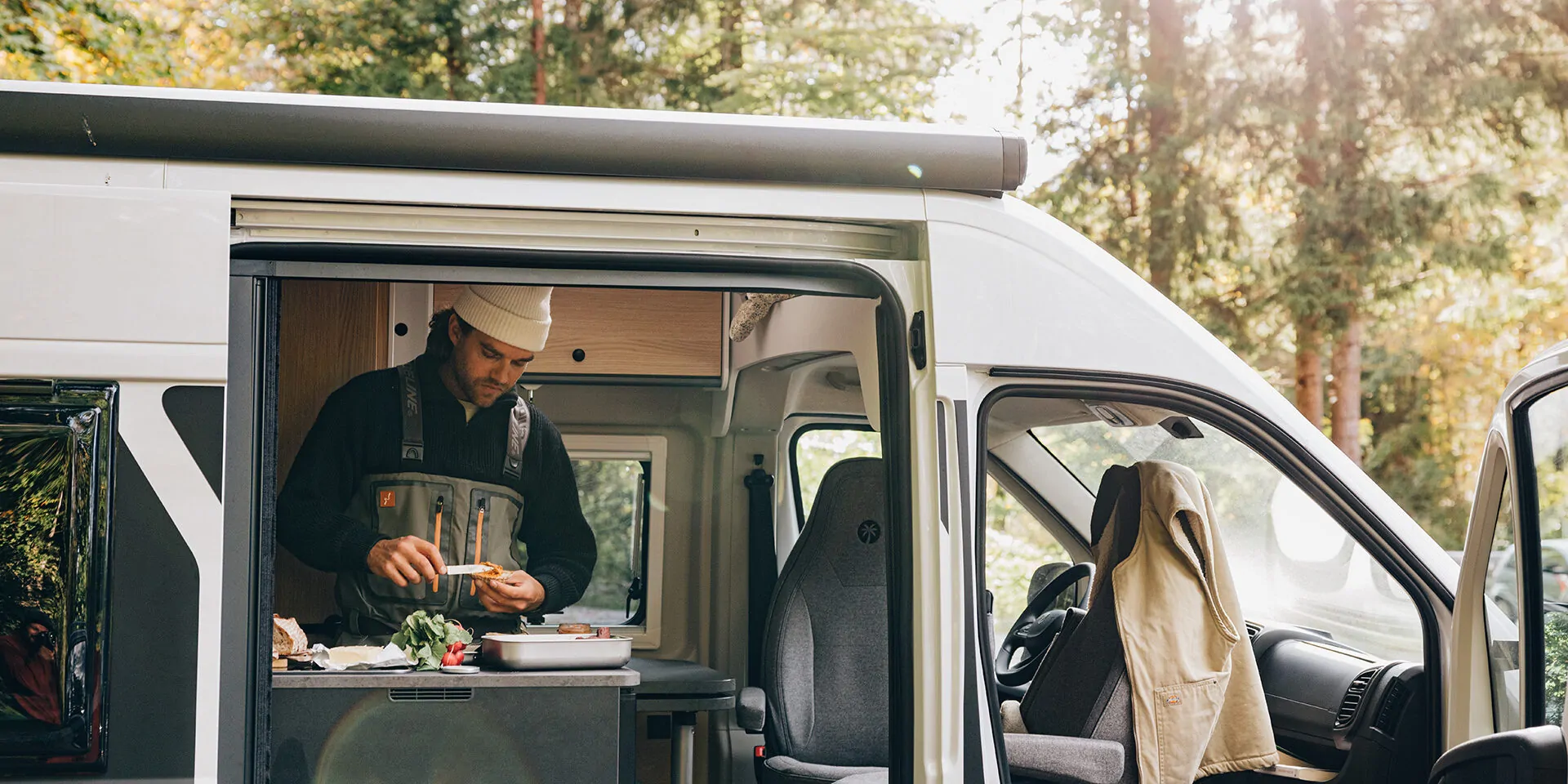 Ein Mann bereitet Essen in einem Campervan vor, während die Schiebetür offen ist.