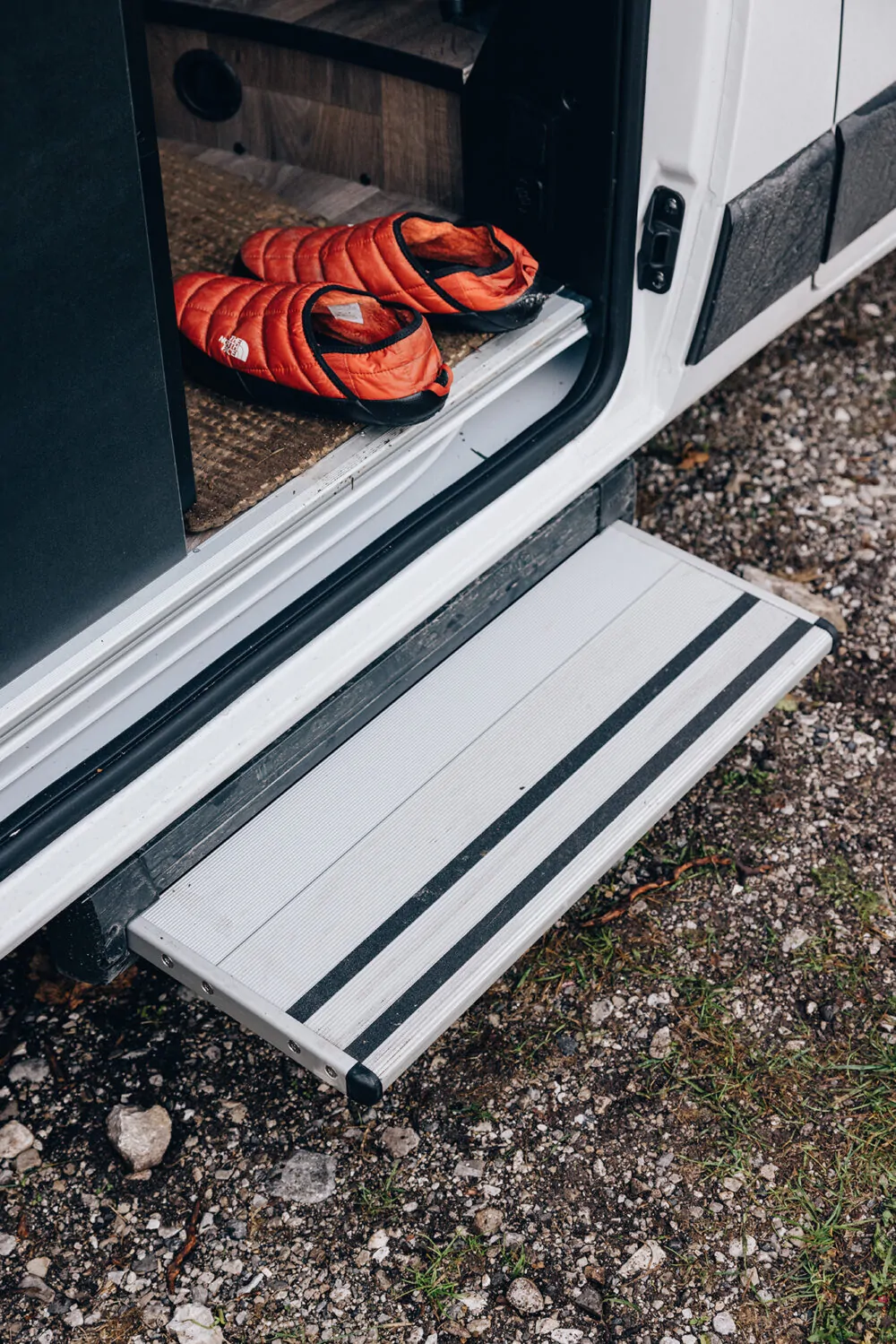Eine ausziehbare Trittstufe eines Campers mit roten Hausschuhen darauf.