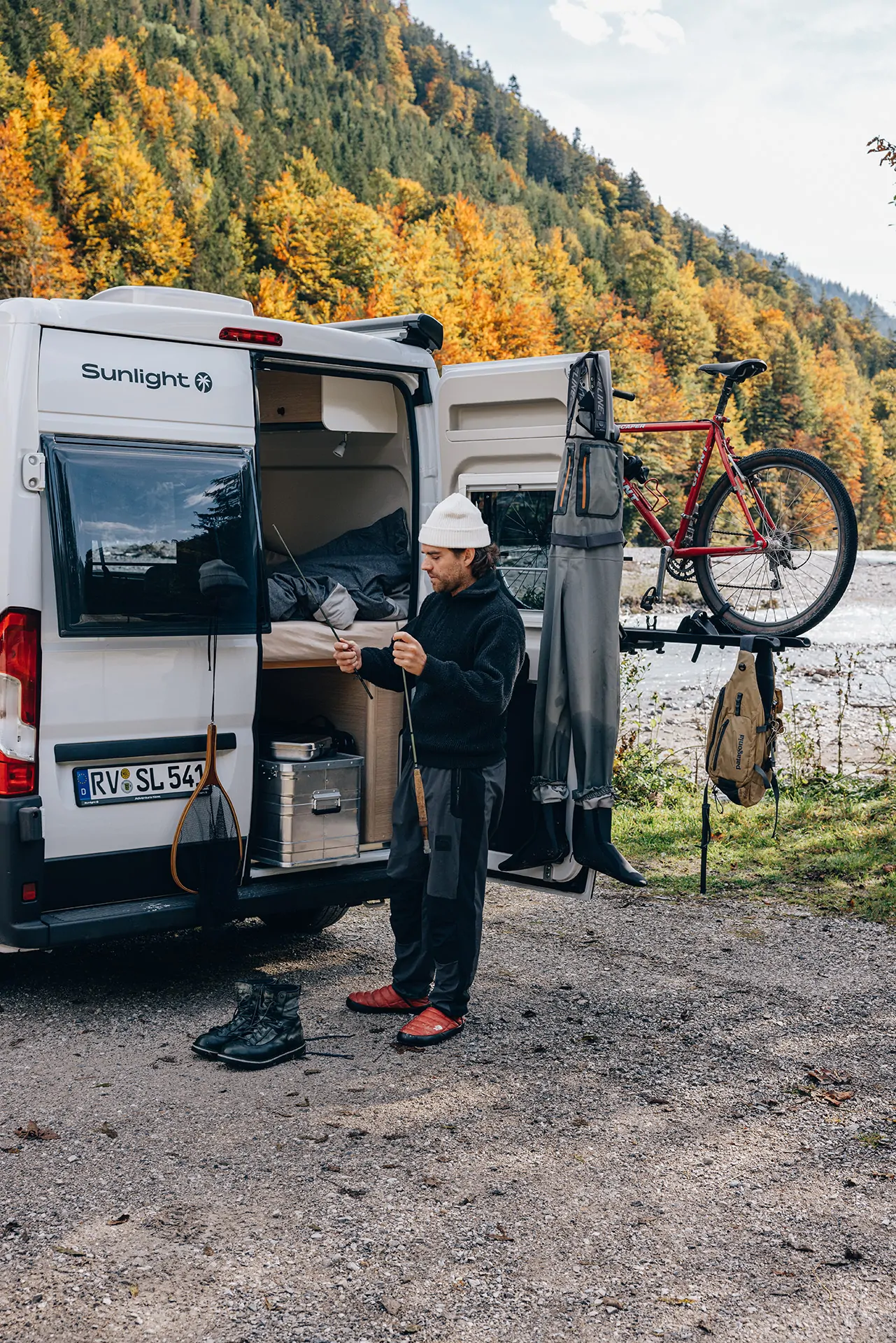Ein Mann steht neben einem Sunlight-Campervan und bereitet Angelausrüstung vor, mit einem Fahrrad am Heck.