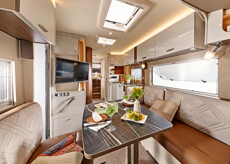 Innenansicht eines modernen Wohnmobils mit Essbereich, Küche und TV.
