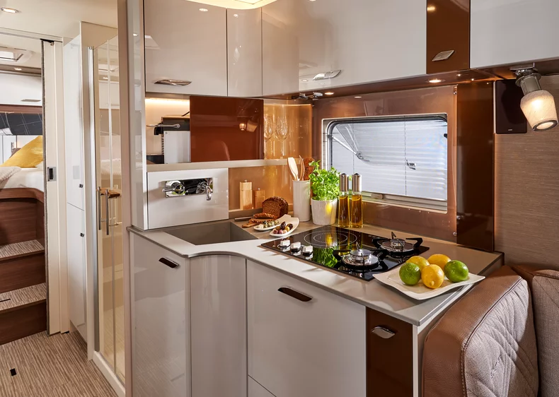 Innenansicht einer modernen Wohnmobilküche mit Herd, Spüle und frischen Zutaten.